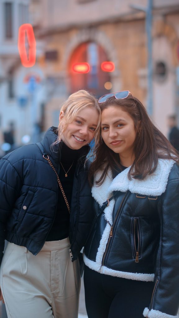 two women standing next to each other in front of a building