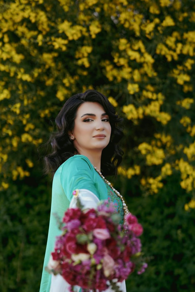uzbekistan woman holding a bouquet of flowers in front of a bush