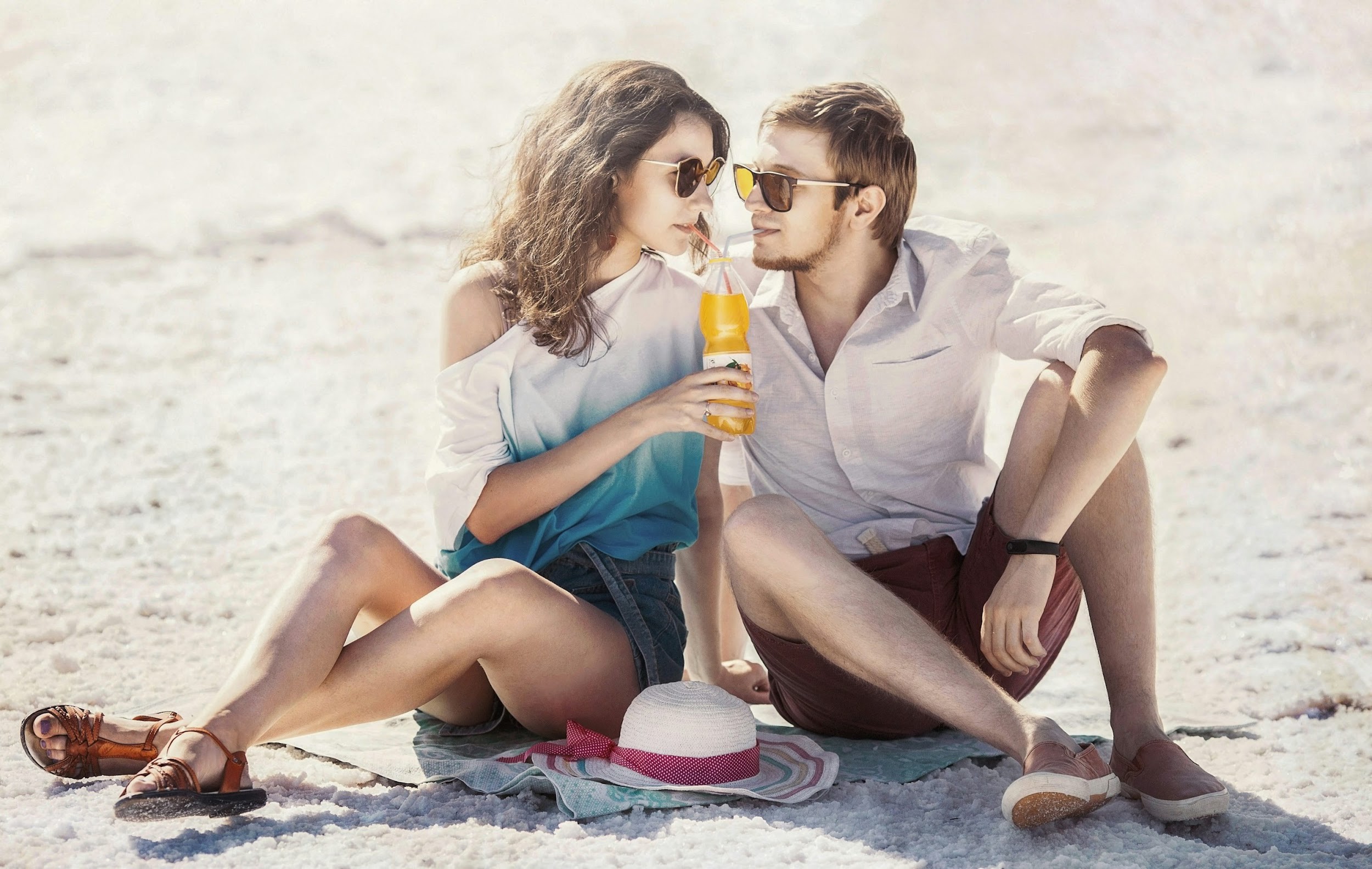 a man and a woman sitting on the beach drinking orange juice