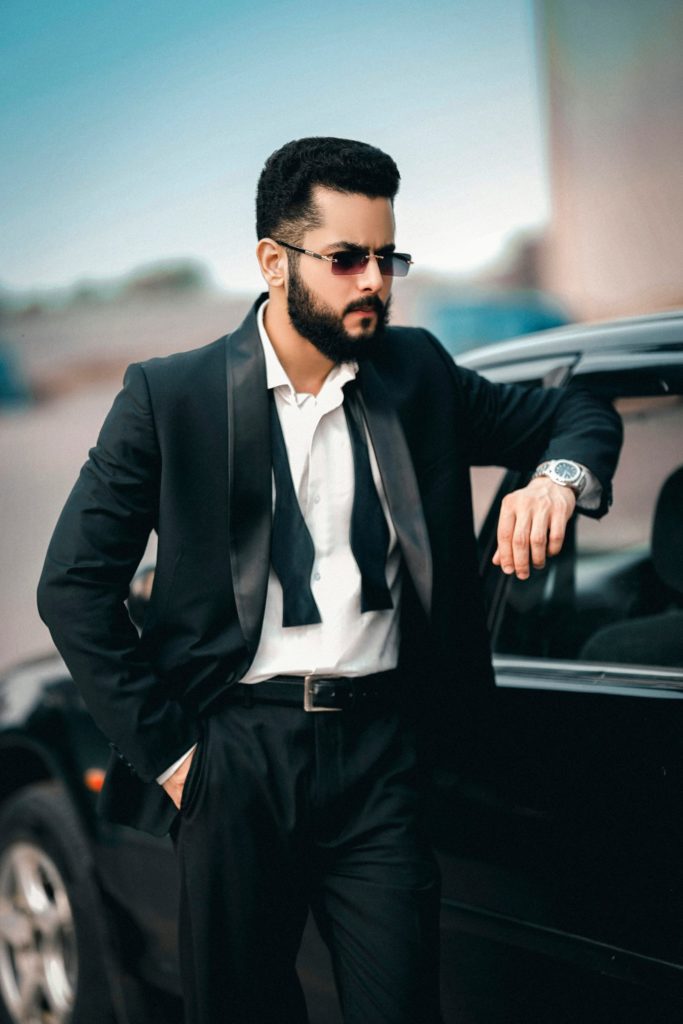 A man in a suit leaning against a car